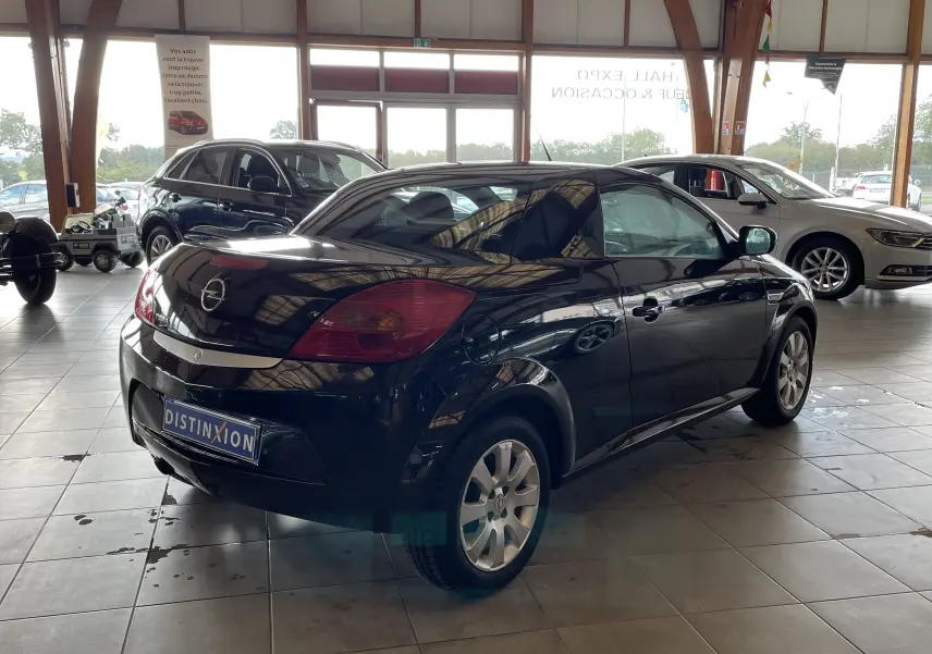 Opel Tigra Twintop noir vue 3/4 arrière droit dans un showroom, toit rigide fermé et jantes alliage visibles.