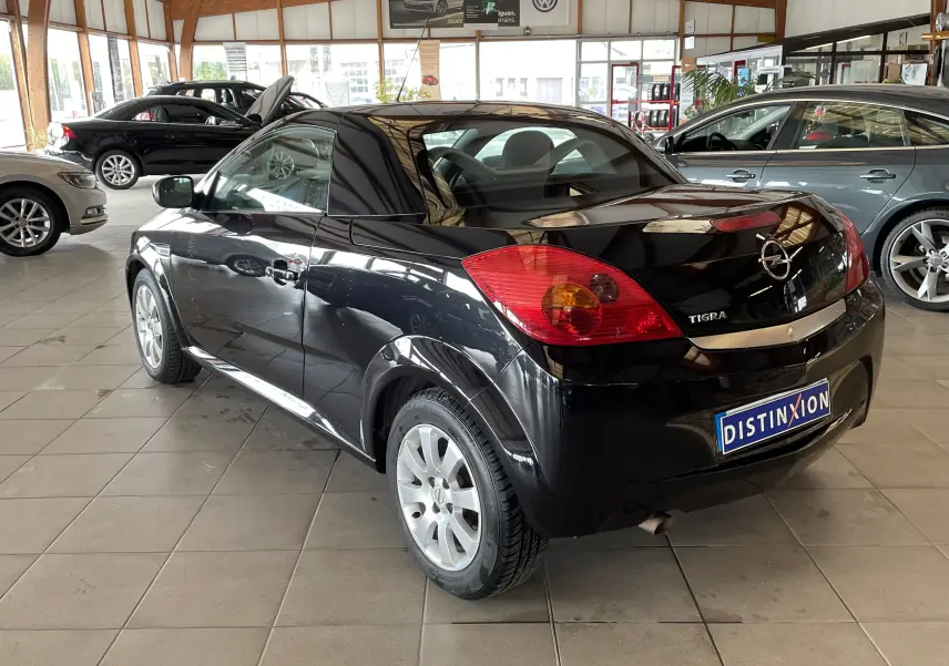 Vue 3/4 arrière droite d'une Opel Tigra Twintop noire de 2006, compacte et brillante, en showroom avec plaque Distinxion.