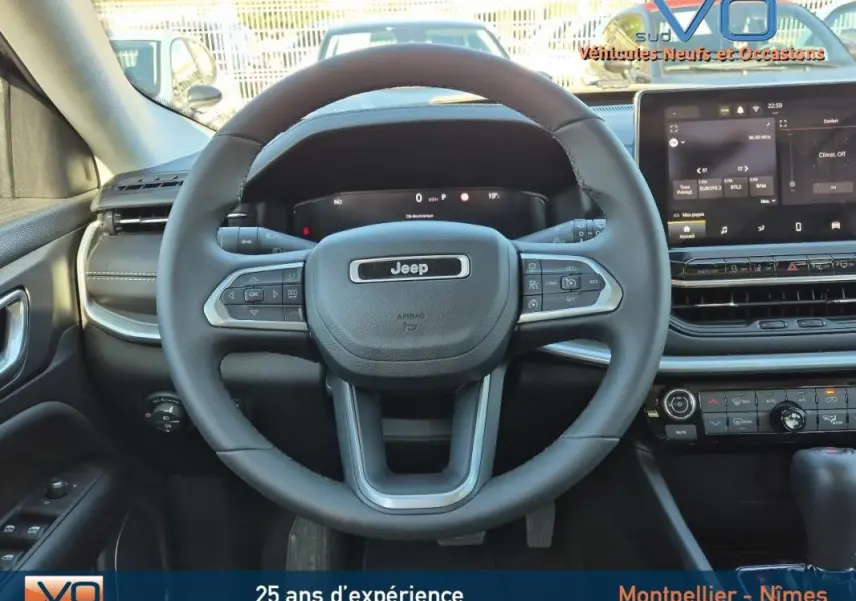 Vue intérieure centrée sur le volant Jeep Compass gris 2024 avec écran tactile et commandes au volant visibles.