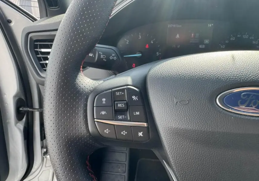 Gros plan sur le volant perforé noir avec surpiqûres rouges et commandes multifonctions de la Ford Focus IV ST-Line.