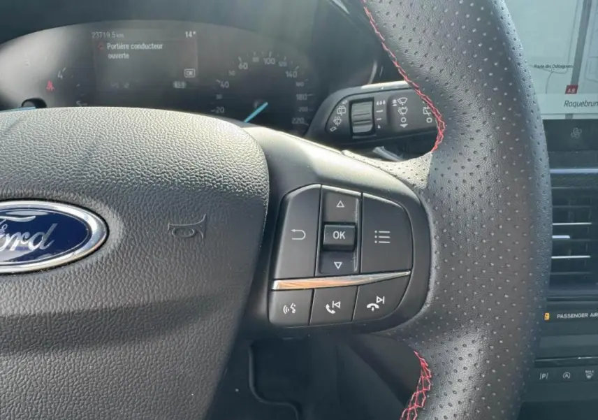 Gros plan sur le volant perforé avec surpiqûres rouges de la Ford Focus IV gris Moondust, affichage numérique visible.