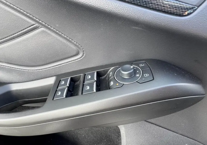 Gros plan sur la commande des vitres et rétroviseurs côté conducteur en plastique noir dans l’habitacle gris du Ford Focus ST-Line.