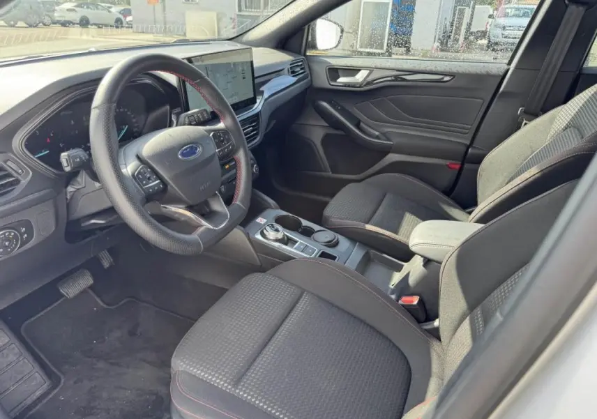 Vue intérieure côté conducteur de la Ford Focus IV ST-Line avec sellerie tissu noire et surpiqûres rouges.
