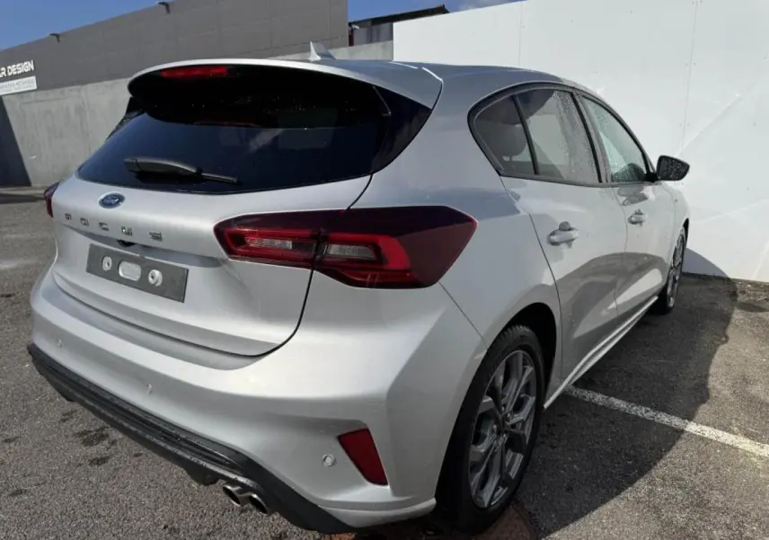 Vue 3/4 arrière droite d'une Ford Focus IV gris Moondust métallisé avec jantes alliage et double sortie d'échappement sport.