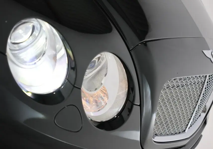 Gros plan sur l'avant droit vert foncé du Bentley Continental Flying Spur, mettant en valeur ses phares ronds et sa calandre chromée.