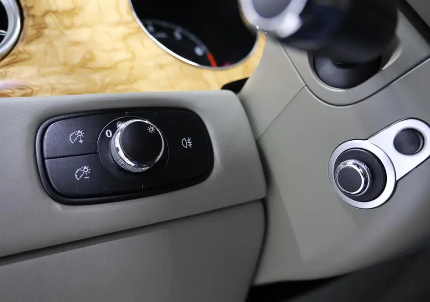 Détail intérieur montrant les commandes d’éclairage sur un tableau de bord beige avec insert bois clair d’une Bentley Continental Flying Spur.