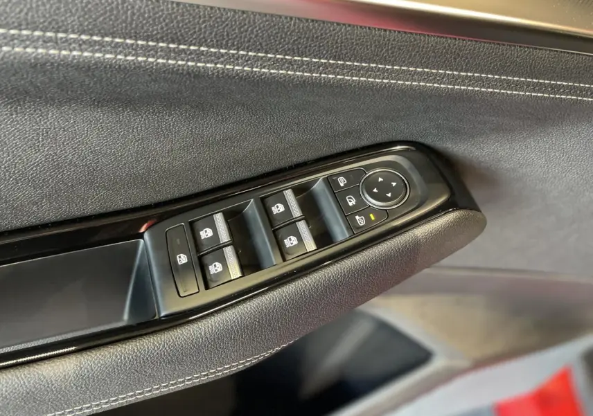 Détail des commandes de lève-vitres sur la porte côté conducteur d’un Renault Rafale rouge avec surpiqûres argentées.