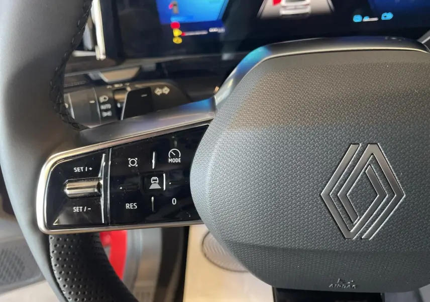 Gros plan sur le volant noir texturé de la Renault Rafale 2025 avec commandes intégrées et logo Renault argenté.