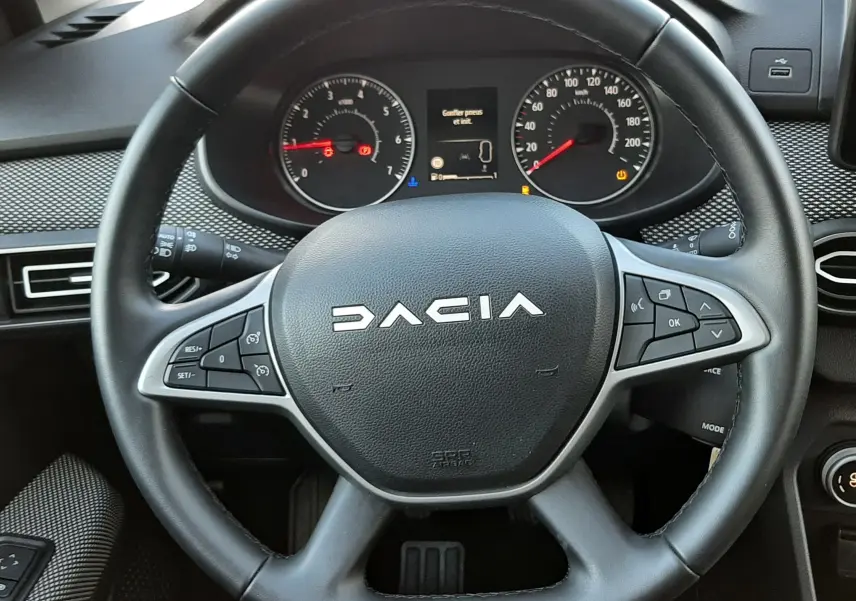 Vue rapprochée du volant noir de la Dacia Jogger 2025 avec tableau de bord et commandes au volant visibles.