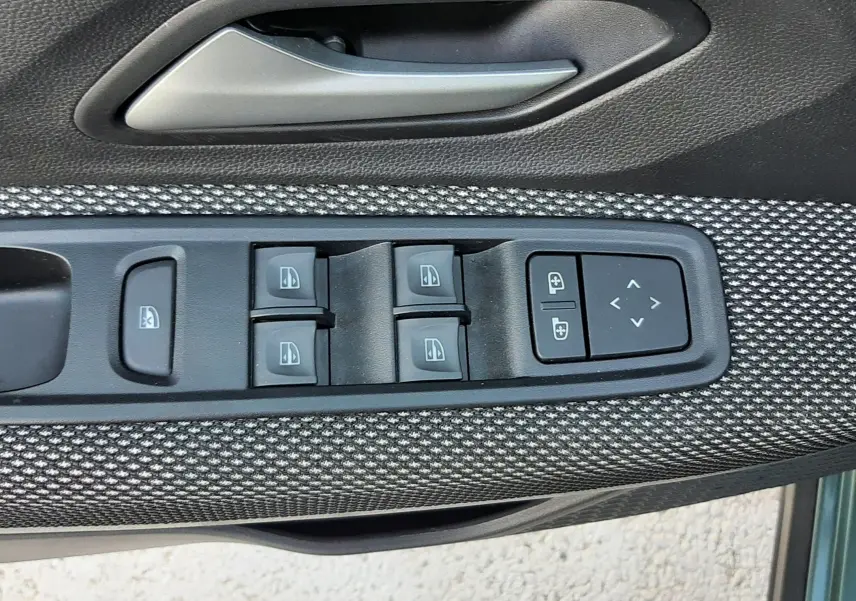 Gros plan sur la commande des vitres électriques et rétroviseurs sur la porte avant gauche du Dacia Jogger vert cèdre métal.