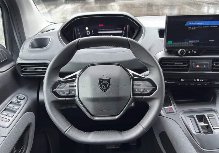 Vue intérieure centrée sur le volant cuir multifonctions du Peugeot Rifter gris Artense avec tableau de bord digital.