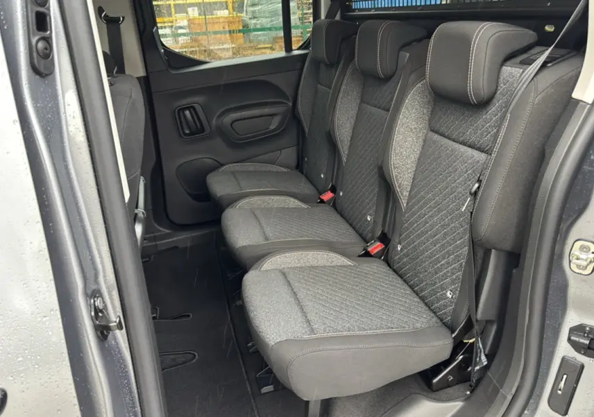 Vue latérale intérieure sur les sièges arrière gris tissu du Peugeot Rifter 2026, porte coulissante ouverte.