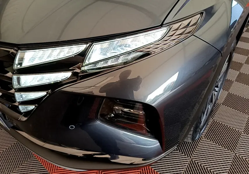 Gros plan sur l'avant droit gris foncé du Hyundai Tucson 1.6 Hybrid 230 avec phares LED et calandre distinctive.