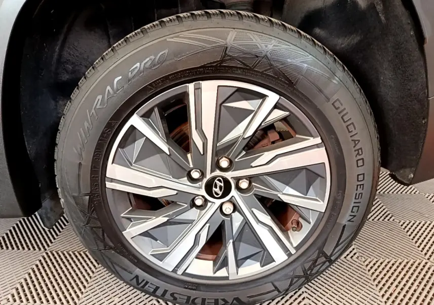 Gros plan sur la roue avant droite du Hyundai Tucson gris foncé, mettant en valeur la jante alu au design géométrique.