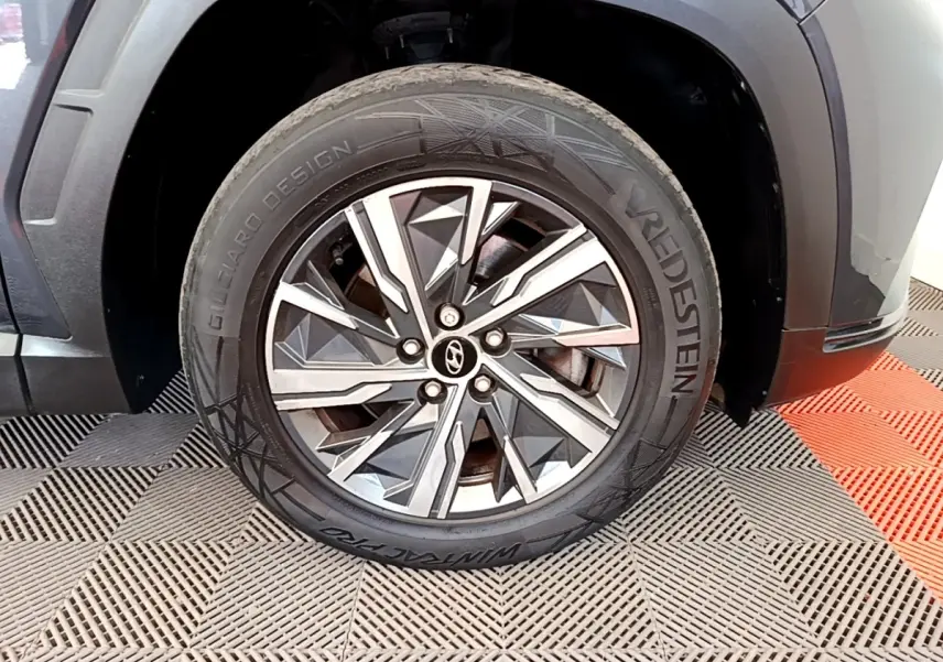 Gros plan sur la roue avant droite d’un Hyundai Tucson gris foncé avec jante alliage au design géométrique.