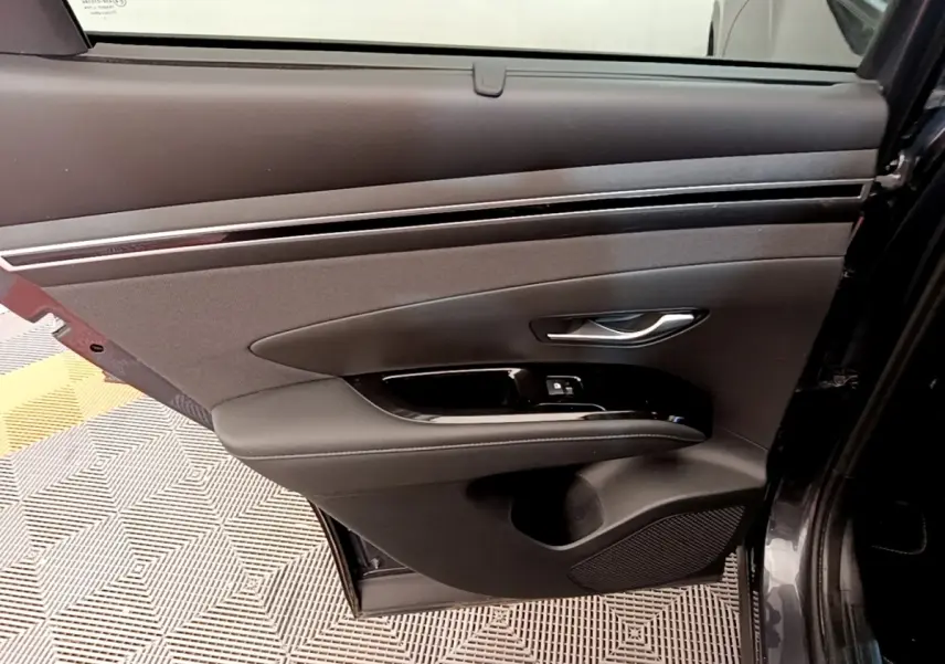 Vue intérieure côté gauche de la porte arrière d'un Hyundai Tucson gris foncé avec garniture noire et commandes de fenêtre.