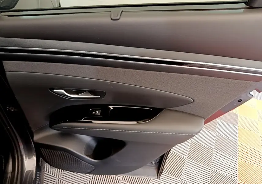 Vue rapprochée de la porte avant gauche gris foncé du Hyundai Tucson 1.6 Hybrid 230 Creative avec garniture noire et poignée argentée.