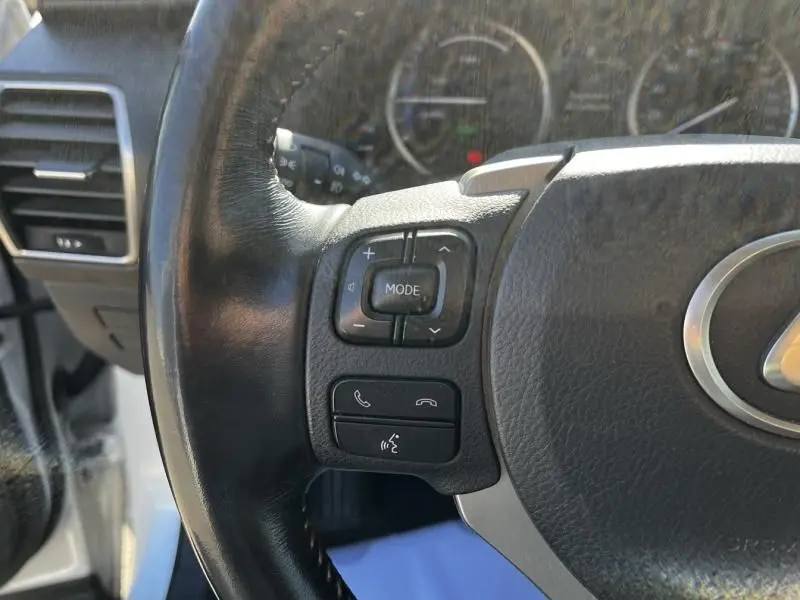 Gros plan sur les commandes gauche du volant en cuir noir du Lexus NX 300H blanc nacré, avec boutons multifonctions visibles.