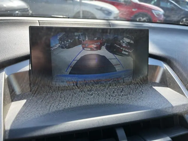Écran intérieur montrant la caméra de recul d'un Lexus NX blanc nacré, avec vue sur des voitures garées derrière.