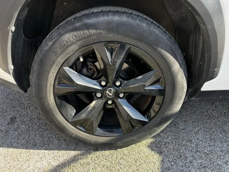 Gros plan sur la roue avant droite du Lexus NX 300H blanc nacré, avec jante noire brillante et logo Lexus central.