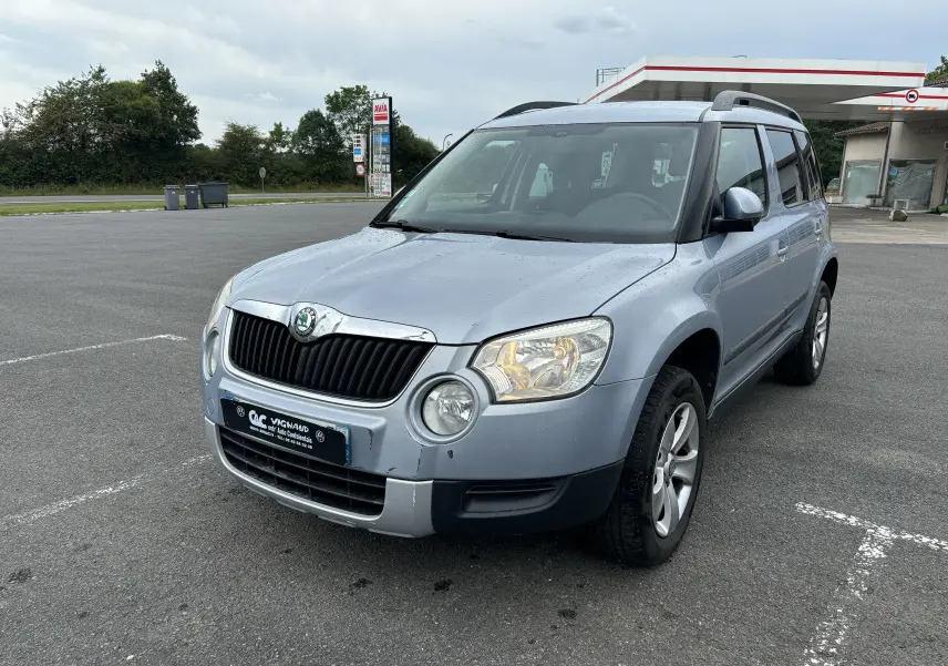Vue 3/4 avant droite d'un Skoda Yeti gris 2012 avec calandre noire et jantes alliage, stationné sur un parking.