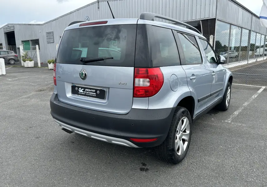 Vue 3/4 arrière droite d'un Skoda Yeti gris 2012 avec hayon noir et jantes alliage sur parking.