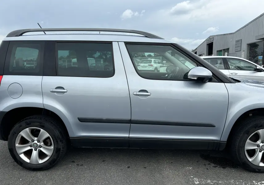 Profil côté droit d'un Skoda Yeti gris de 2012 avec barres de toit et jantes alliage visibles.