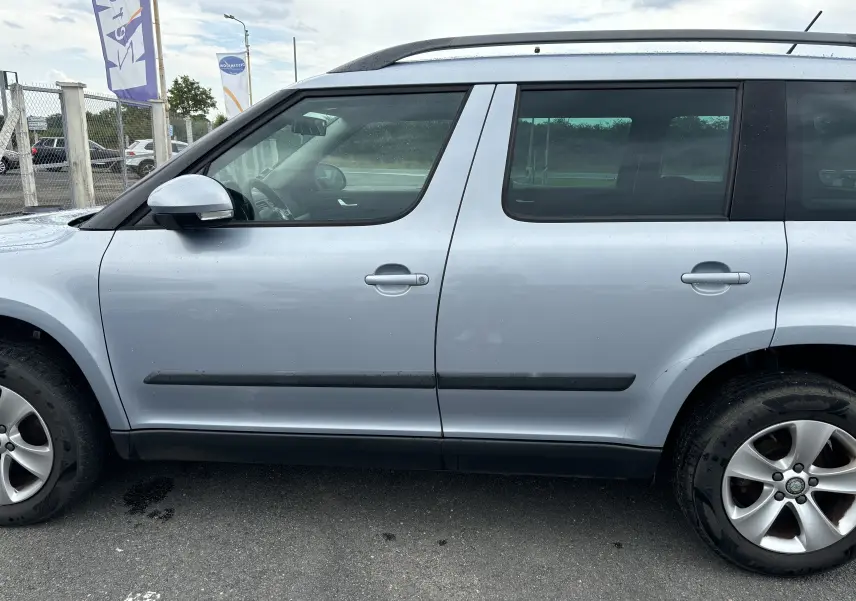 Profil côté gauche d'un Skoda Yeti gris 2012, version Ambition, avec jantes alliage et barres de toit noires.
