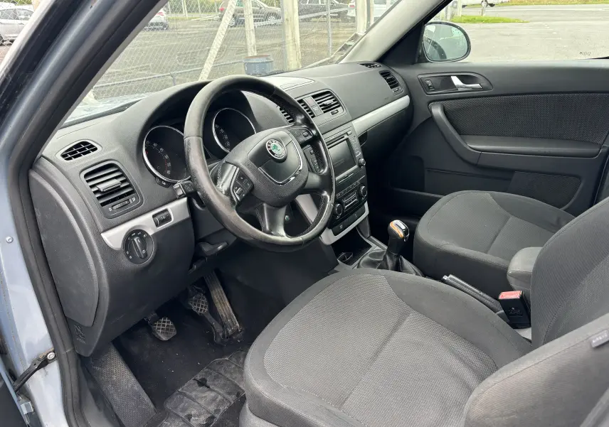 Intérieur côté conducteur du Skoda Yeti gris 2012, montrant le volant, tableau de bord et sièges en tissu noir.