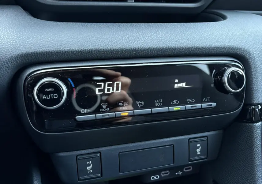 Gros plan sur la console centrale noire de la Toyota Yaris 2025, affichant la climatisation automatique à 26°C et les sièges chauffants.