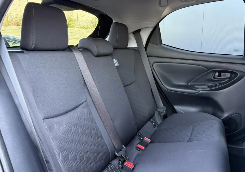 Vue côté droit des sièges arrière en tissu gris foncé de la Toyota Yaris Hybride 2025 avec ceinture de sécurité et porte intérieur noir.