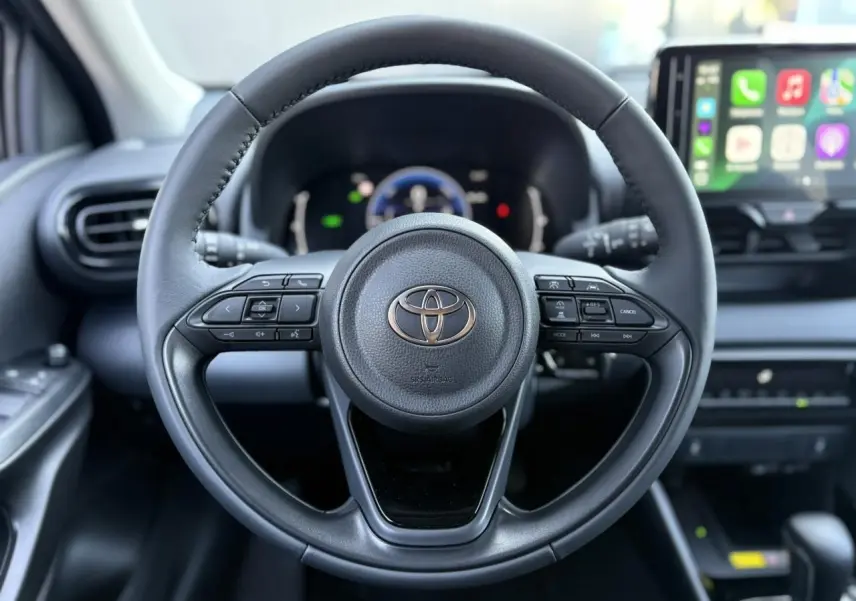 Volant cuir noir de la Toyota Yaris Hybride 2025 avec commandes intégrées et écran tactile multimédia en arrière-plan