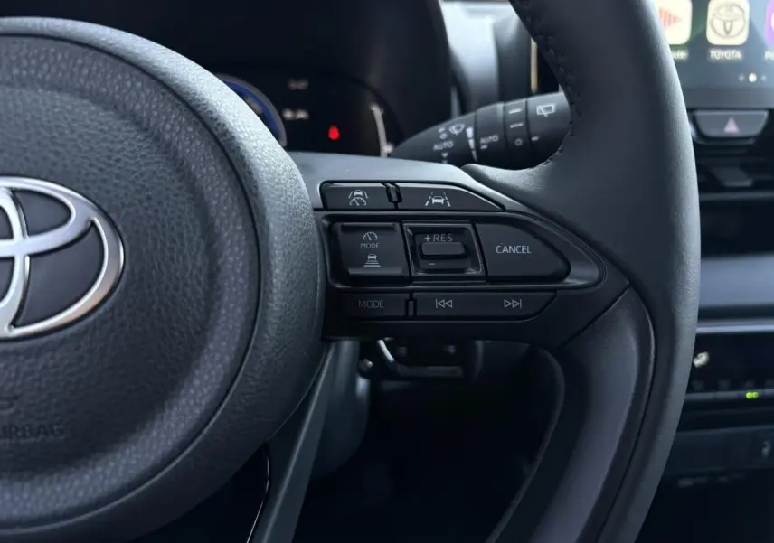 Gros plan sur le volant cuir noir de la Toyota Yaris 2025 hybride, montrant les commandes d’aide à la conduite et multimédia.