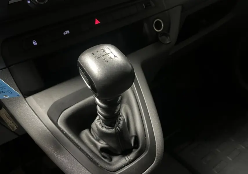 Gros plan sur le levier de vitesses manuel noir du Peugeot Expert Fourgon blanc, avec tableau de bord gris en arrière-plan.