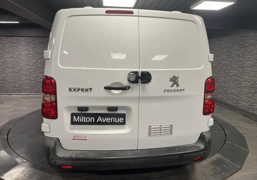 Vue arrière d'un Peugeot Expert Fourgon blanc avec portes battantes et bouclier noir dans un showroom.