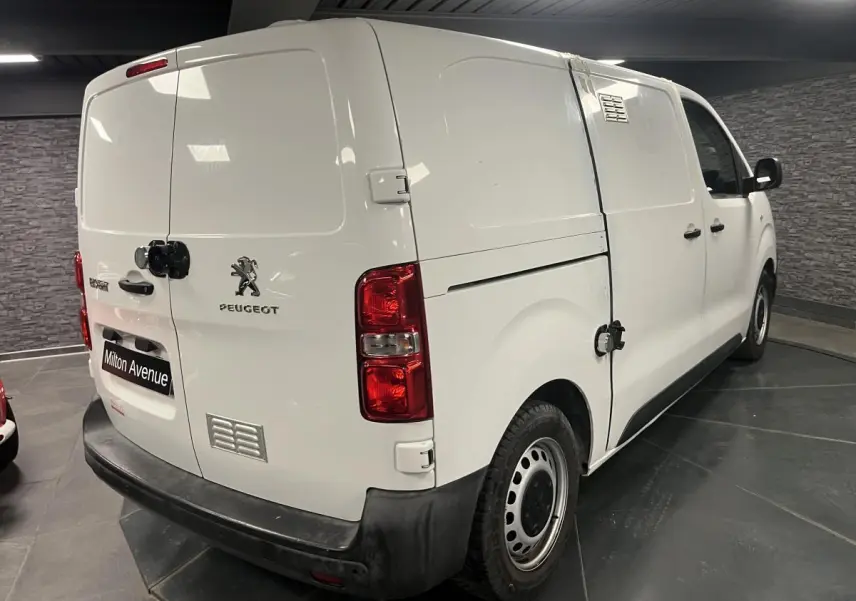 Vue 3/4 arrière droite d'un Peugeot Expert Fourgon blanc avec boucliers noirs et portes tôlées en intérieur showroom.