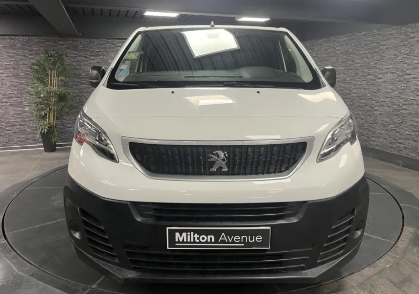 Vue frontale d'un Peugeot Expert Fourgon blanc avec boucliers noirs et calandre noire en intérieur showroom.