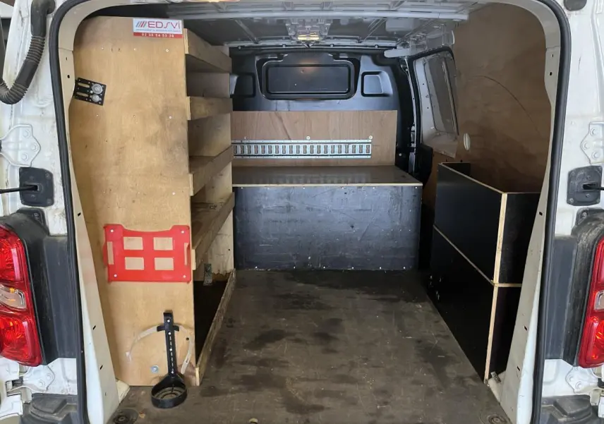Vue arrière du Peugeot Expert Fourgon blanc 2020 montrant l'intérieur utilitaire avec étagères et plancher bois antidérapant.
