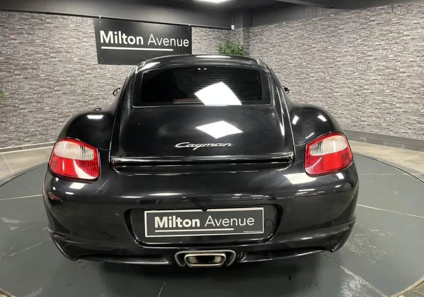 Vue arrière d'une Porsche Cayman noire 2008 avec feu arrière rouge et sortie d'échappement centrale visible.