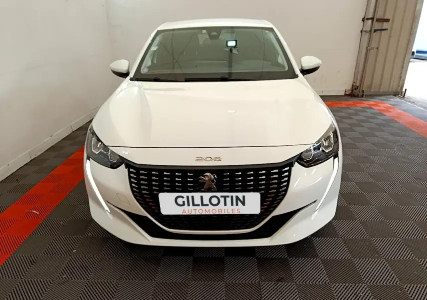 Vue avant d'une Peugeot 208 blanche 2020 avec calandre noire et feux LED, stationnée sur sol à damier gris et rouge.