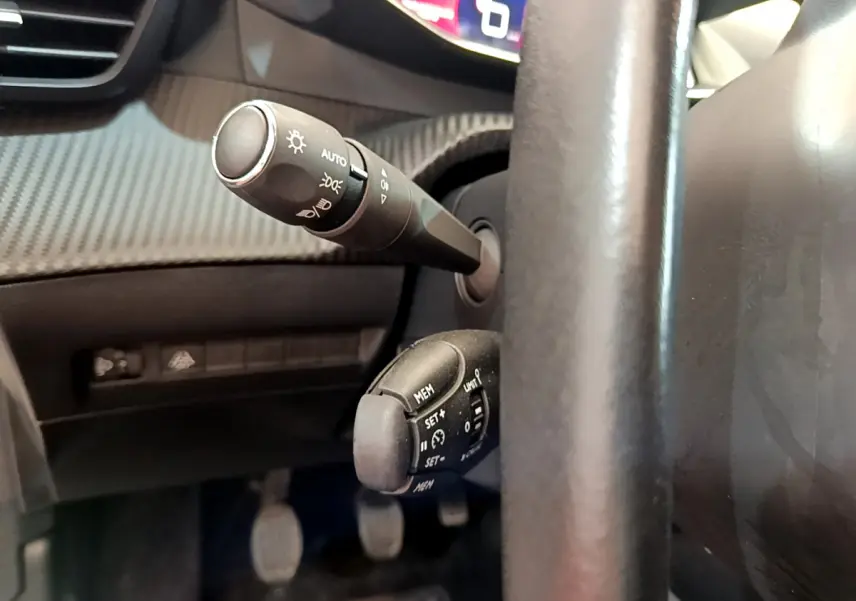 Gros plan sur les commandes au volant et le tableau de bord numérique d'une Peugeot 208 blanche, version PureTech 100 S&S Allure Business.