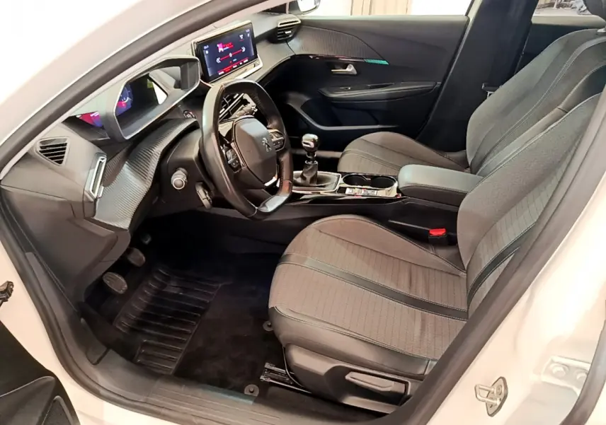 Intérieur côté conducteur d'une Peugeot 208 blanche, avec tableau de bord numérique et sièges tissu gris.