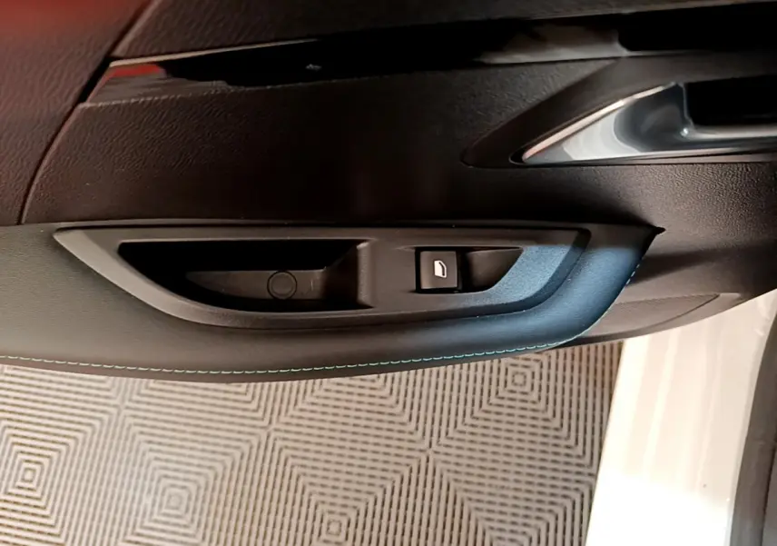 Gros plan sur la poignée intérieure et le bouton de lève-vitre côté gauche d'une Peugeot 208 blanche 2020.