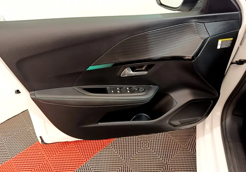 Vue côté gauche de la porte avant blanche d'une Peugeot 208 2020, avec garniture noire et insert effet carbone.