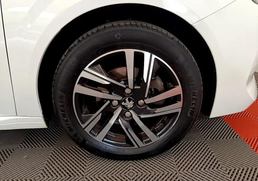 Gros plan sur la roue avant gauche blanche d'une Peugeot 208 avec jante alliage noire et argentée au design moderne.