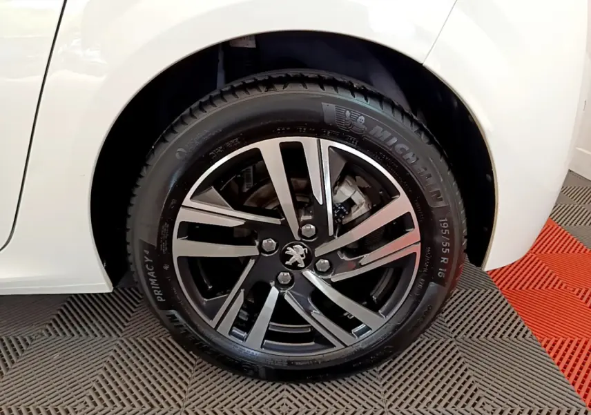 Gros plan sur la roue avant gauche d'une Peugeot 208 blanche avec jante alliage noire et argentée.