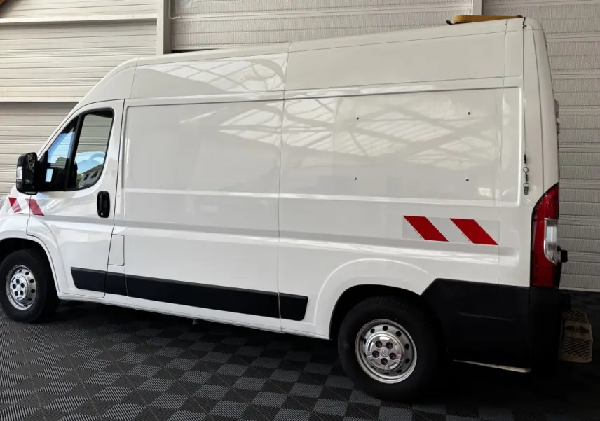 Vue de profil côté gauche d’un utilitaire Citroën Jumper blanc avec bandes réfléchissantes rouges et jantes acier.
