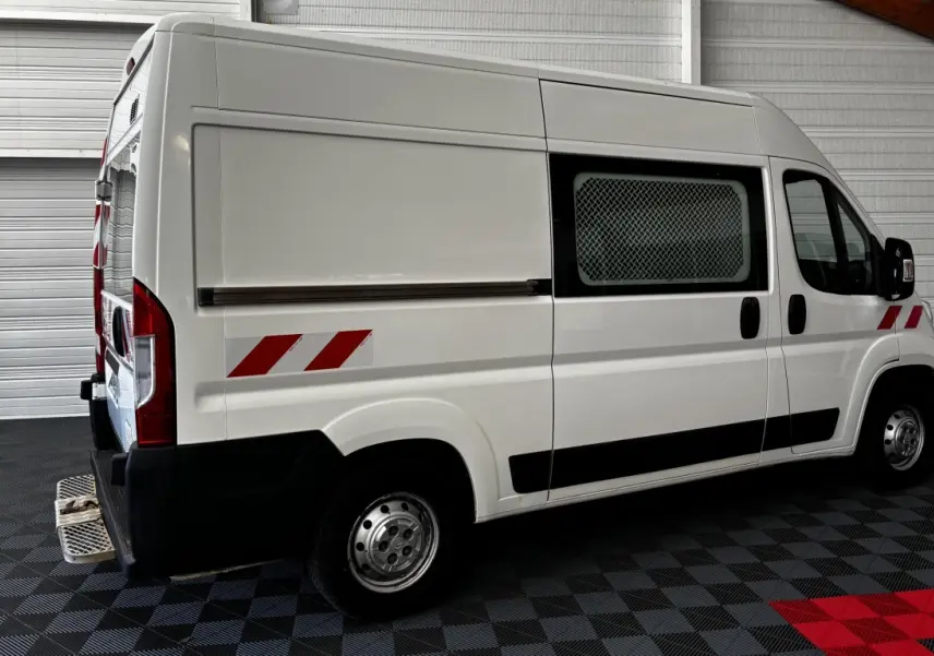 Vue latérale droite d’un utilitaire blanc Citroën Jumper 35 L2H2 avec marquages réfléchissants rouges et grille de protection sur la fenêtre.