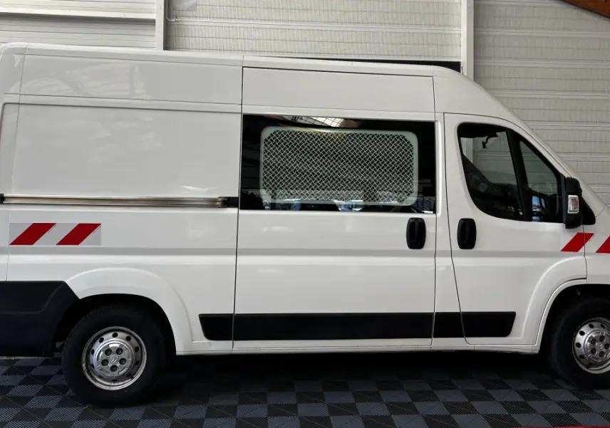 Vue latérale droite d’un utilitaire blanc Citroën Jumper 35 L2H2 avec marquages rouges et grille de protection sur la fenêtre.