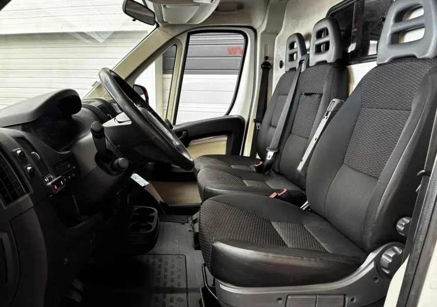 Vue intérieure côté conducteur du Citroën Jumper blanc, montrant le volant multifonctions et les trois sièges avant en tissu noir.